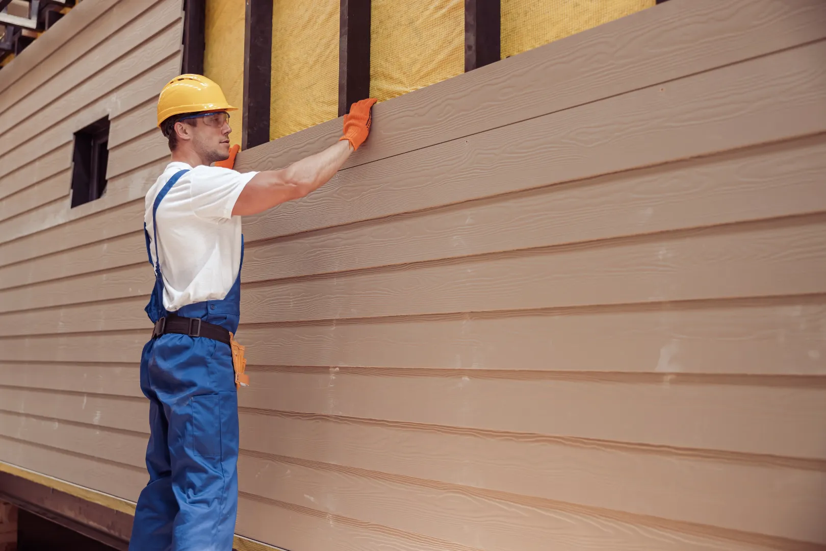 A man installing fiber cement siding on a house